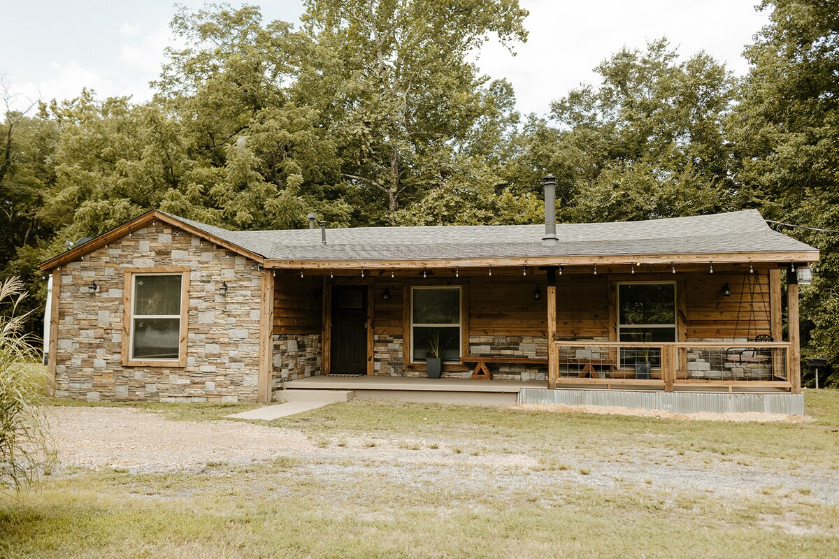 Front exterior of Running Water Cabin with a covered porch and wooded backdrop